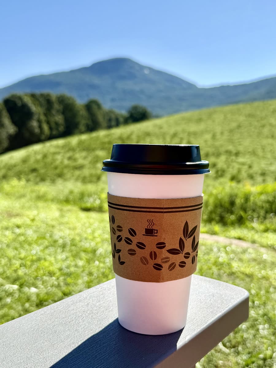 A JumpinGoat coffee in a kraft sleeve resting on a railing, with Mount Yonah rising in the background.